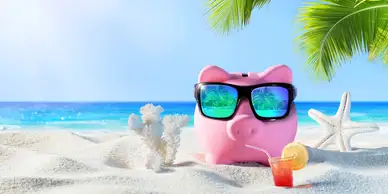 A pink piggy bank with sunglasses on the beach.