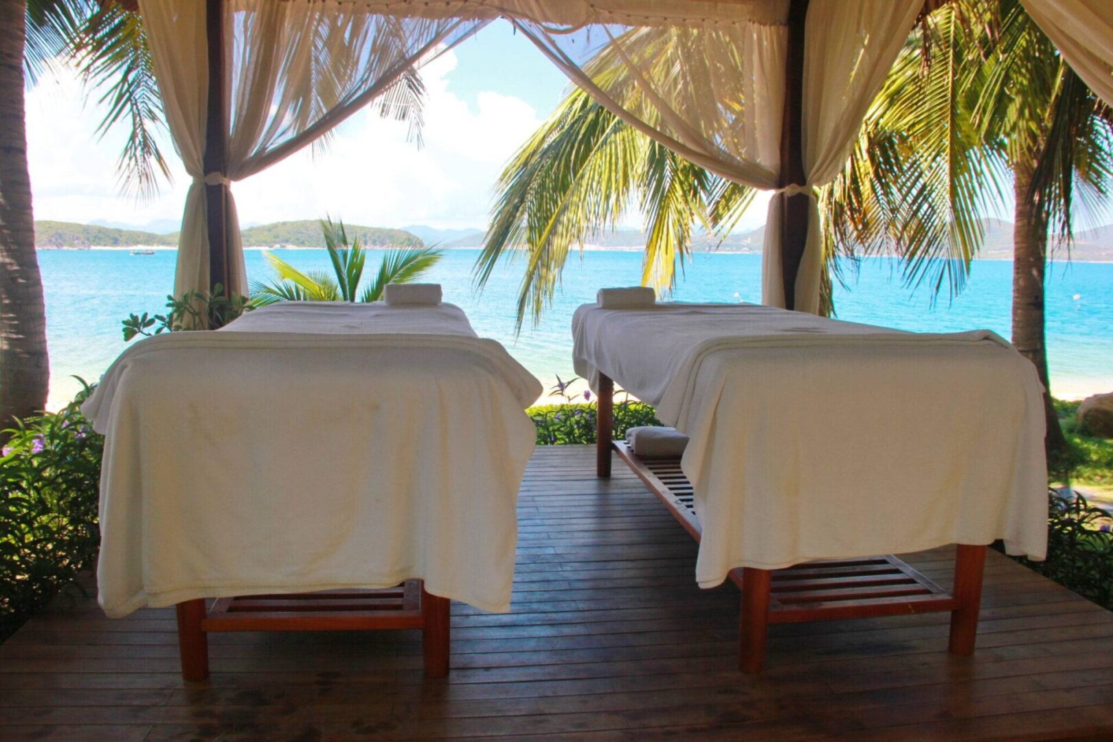 Two beds in a room with curtains and palm trees.